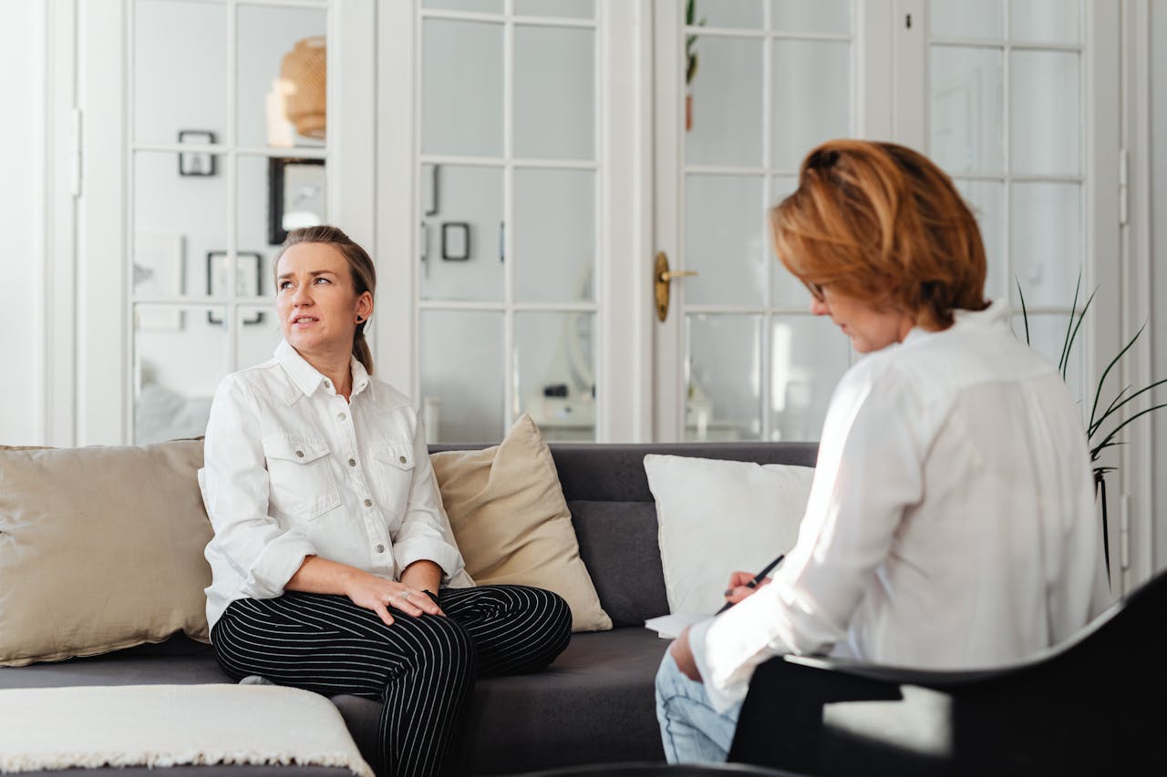 services-04 Two women engaging in a counseling session on a sofa inside a modern room.