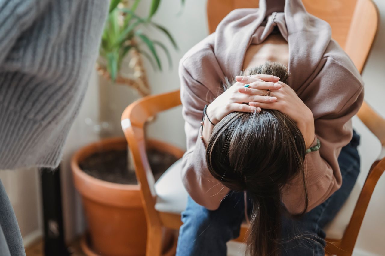 services-03 Faceless upset female with hands behind head sitting on chair while having argument with unrecognizable person in room at home